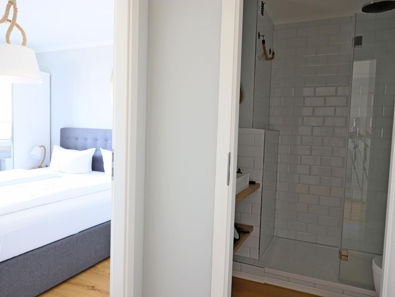 Schlafzimmer mit Bett und Badezimmer mit Dusche und Fliesen