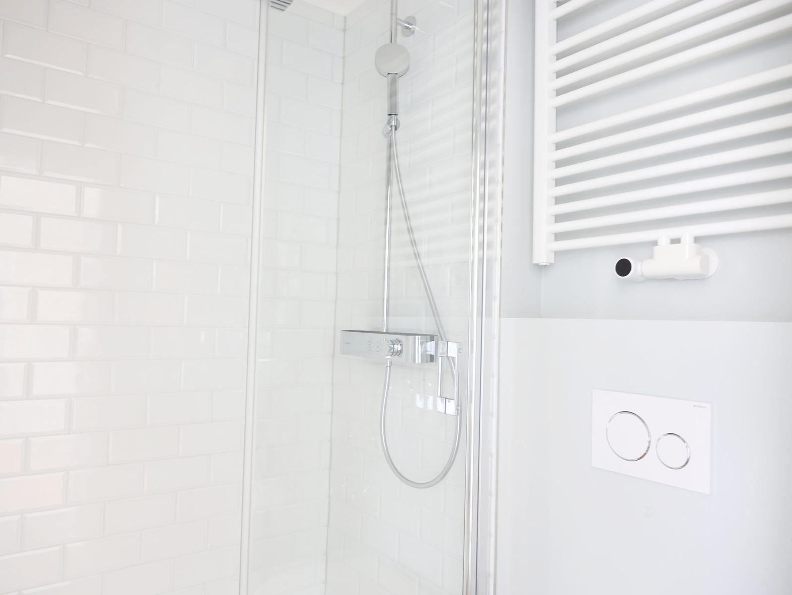 Dusche mit Glaswand, weißen Fliesen und modernem Duschsystem.