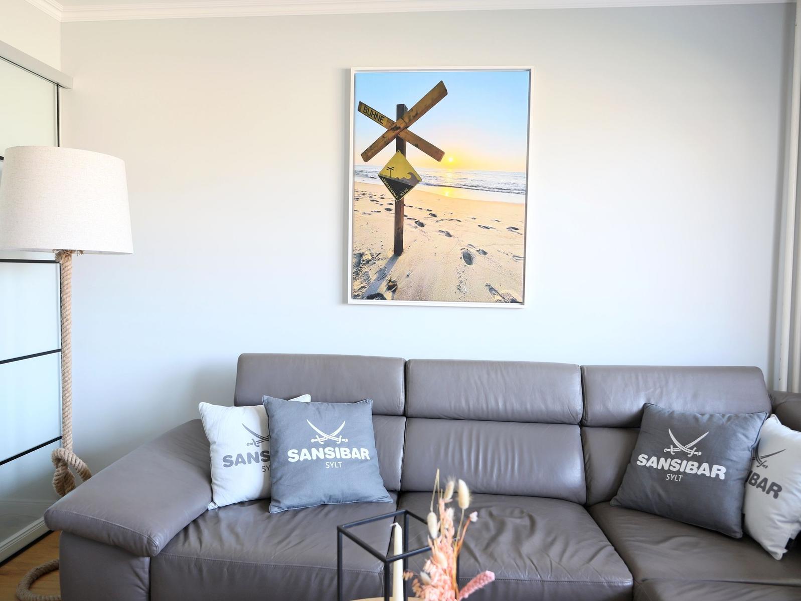 Grauer Sofa mit Kissen und Wandbild mit Strandmotiv.