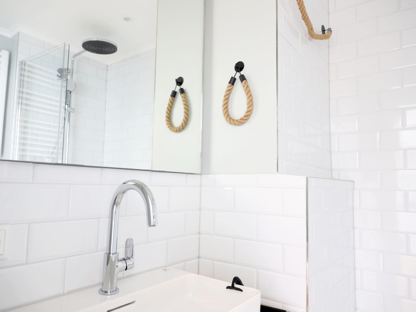 Badezimmer mit weißer Fliesenwand, Spiegel und Seilhaken.
