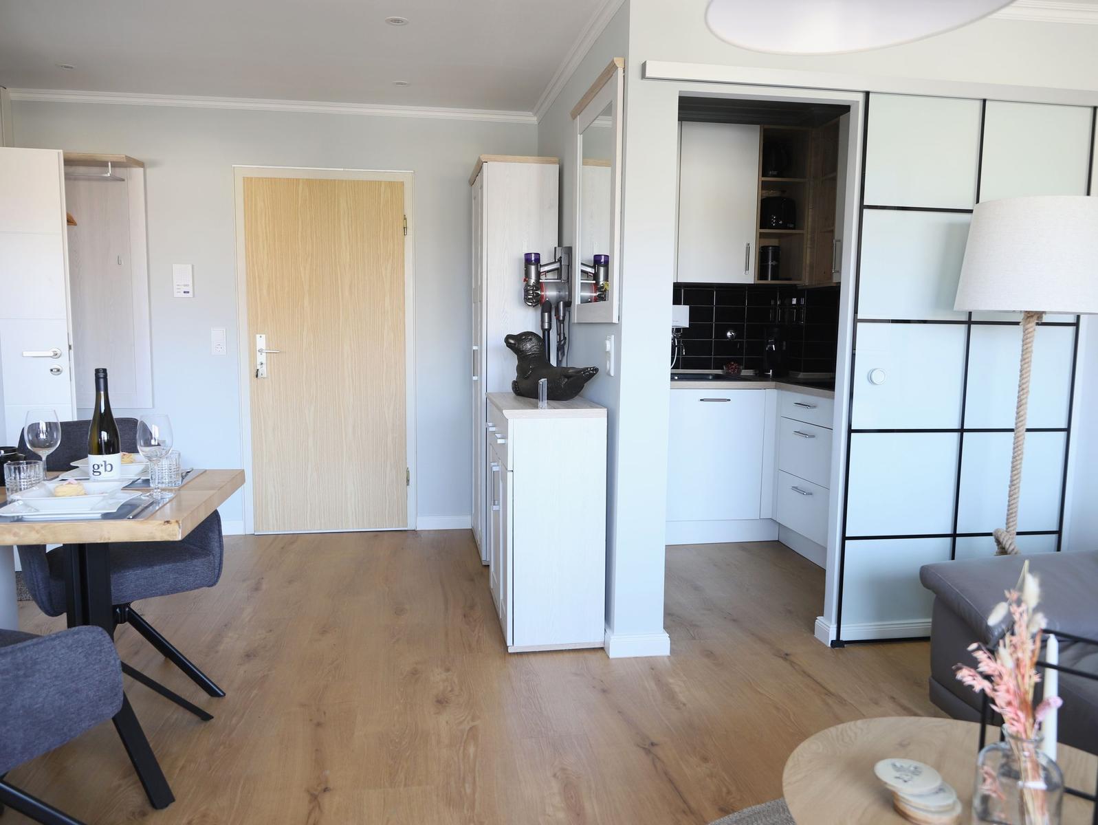 Wohnung mit Essbereich, Küche und Wohnzimmer. Holzboden und weiße Möbel.