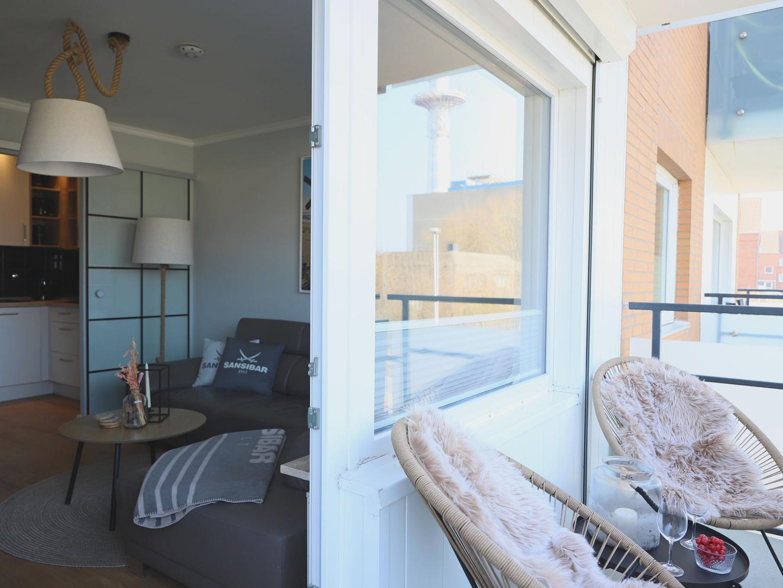 Wohnbereich mit Balkon, Sitzmöbel und Blick auf Stadtlandschaft.