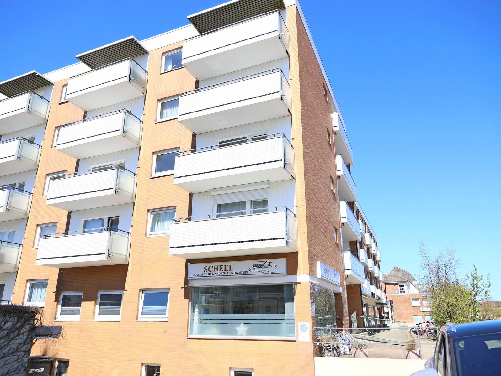 Moderne Mehrfamilienhaus mit Balkonen und Geschäftsfassade unter blauem Himmel.