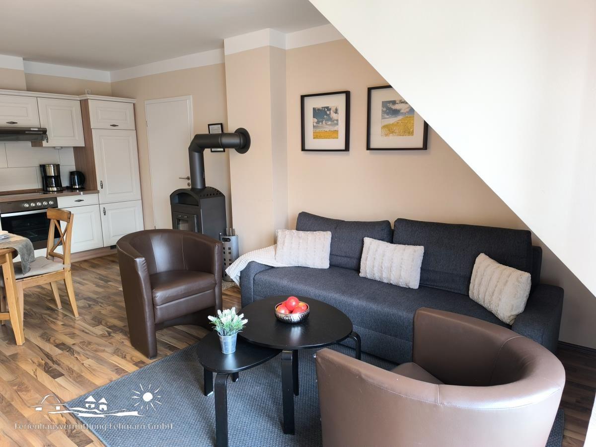 Wohnbereich mit Sofa, zwei Sesseln und Küchenbereich im Hintergrund.