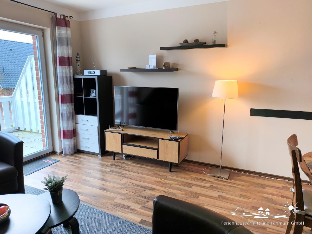 Wohnzimmer mit Fernseher, Holzboden und Balkontür.