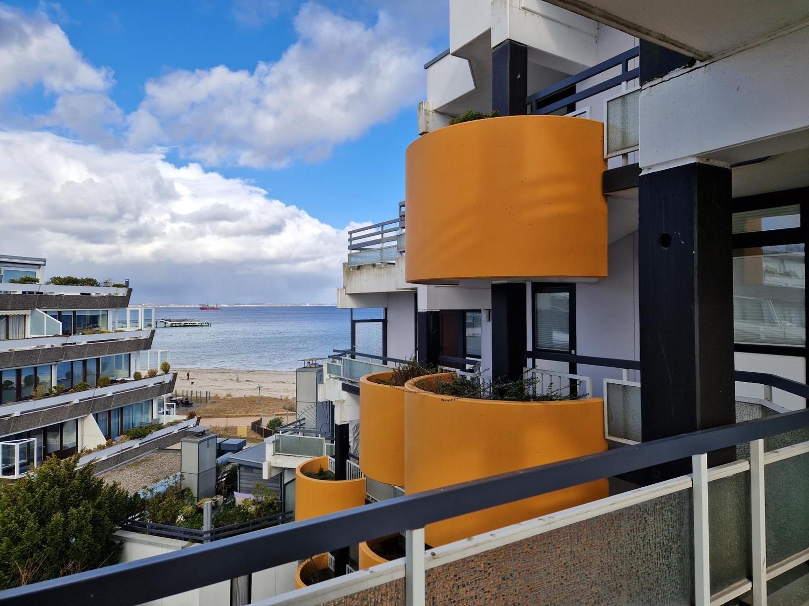 Blick auf das Meer und den Strand von der Terrasse mit orangefarbenen Balkonen.