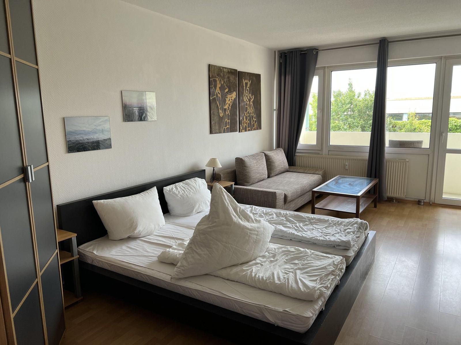 Schlafzimmer mit Bett, Sofa und Fenster zum Balkon.