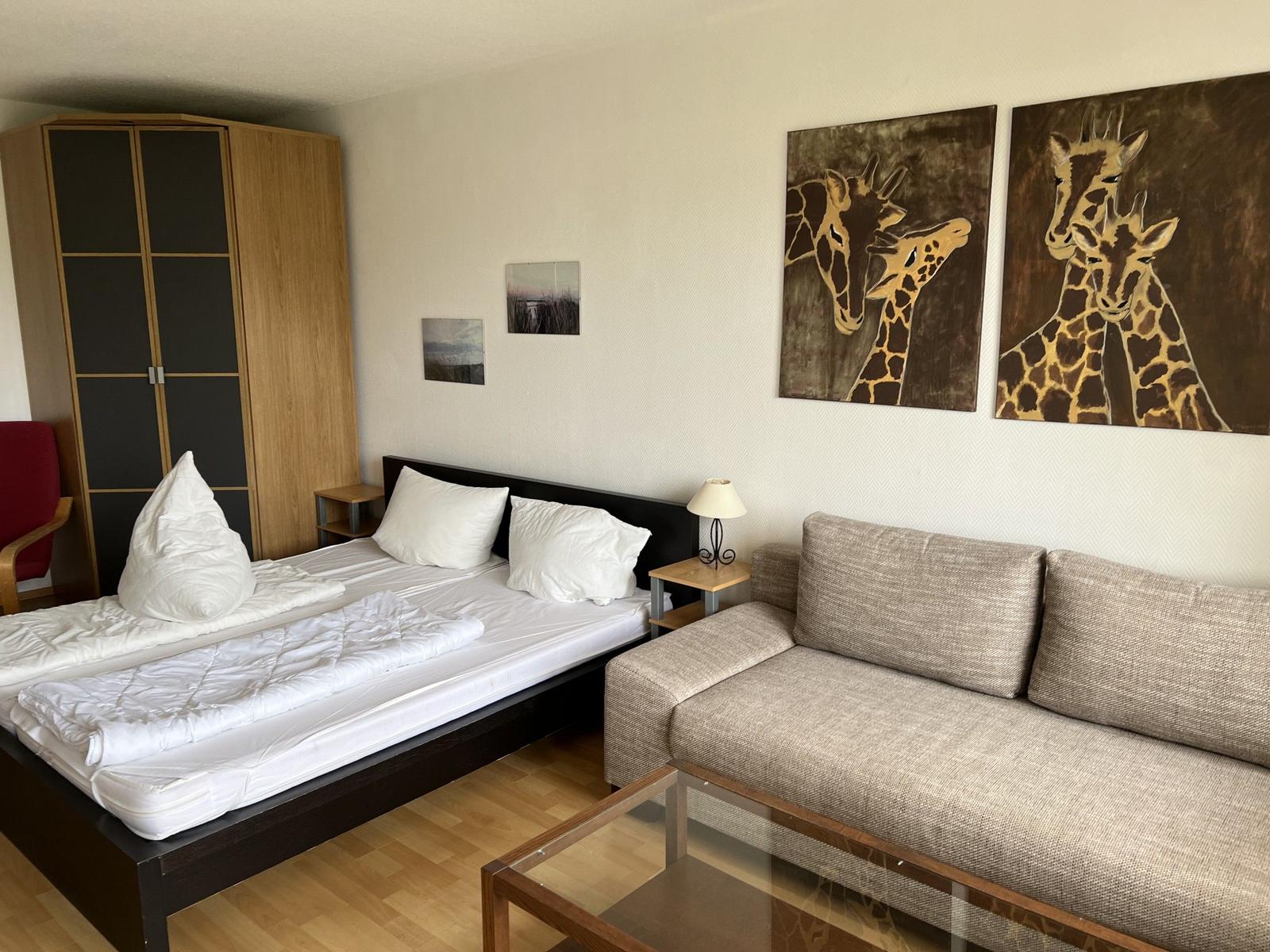 Zimmer mit Bett, Sofa und Giraffenbildern an der Wand.