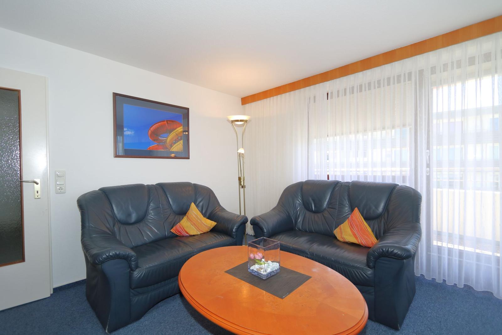Zwei schwarze Ledersofas um einen runden Holztisch mit einer Vase.