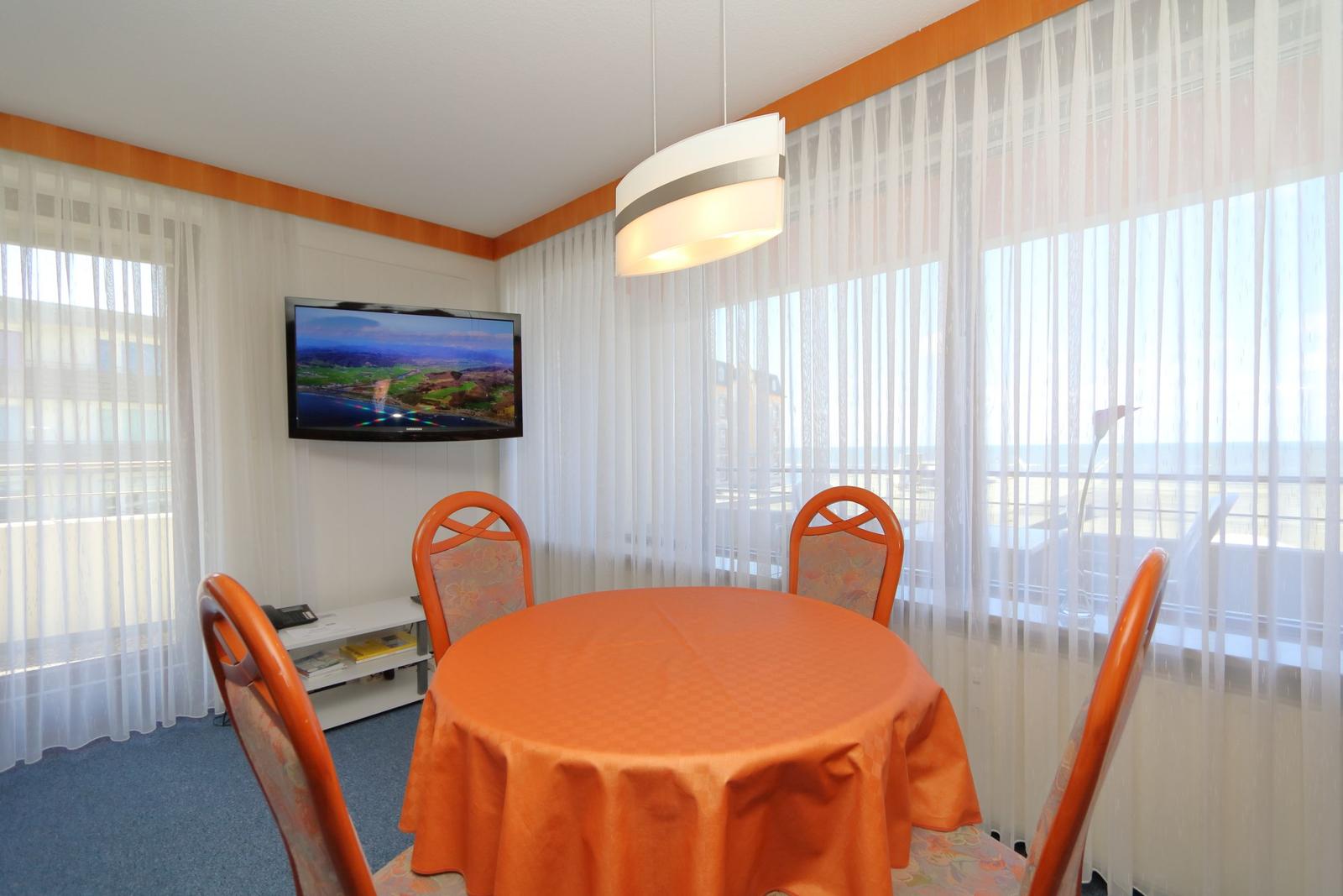 Rundtisch mit vier Stühlen, TV und Fenster mit Blick auf Balkon.