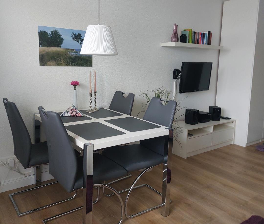 Essbereich mit Tisch, Stühlen und Wandbild. Fernseher auf Möbelwand mit Lautsprechern.
