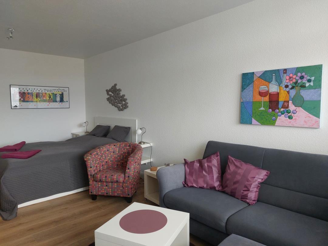 Schlafzimmer mit Bett, Sofa und Stuhl. Wandbilder und Holzboden.