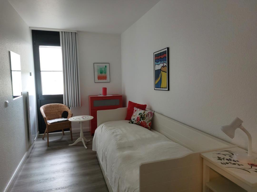 Schlafzimmer mit Bett, Stuhl, Tisch und Wandbildern.