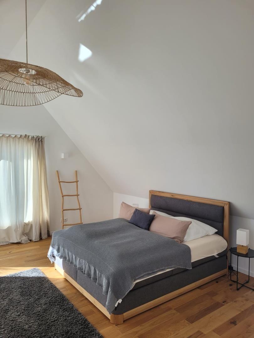 Schlafzimmer mit Dachschrägen, Holzboden und Bett mit grauer Bettdecke.