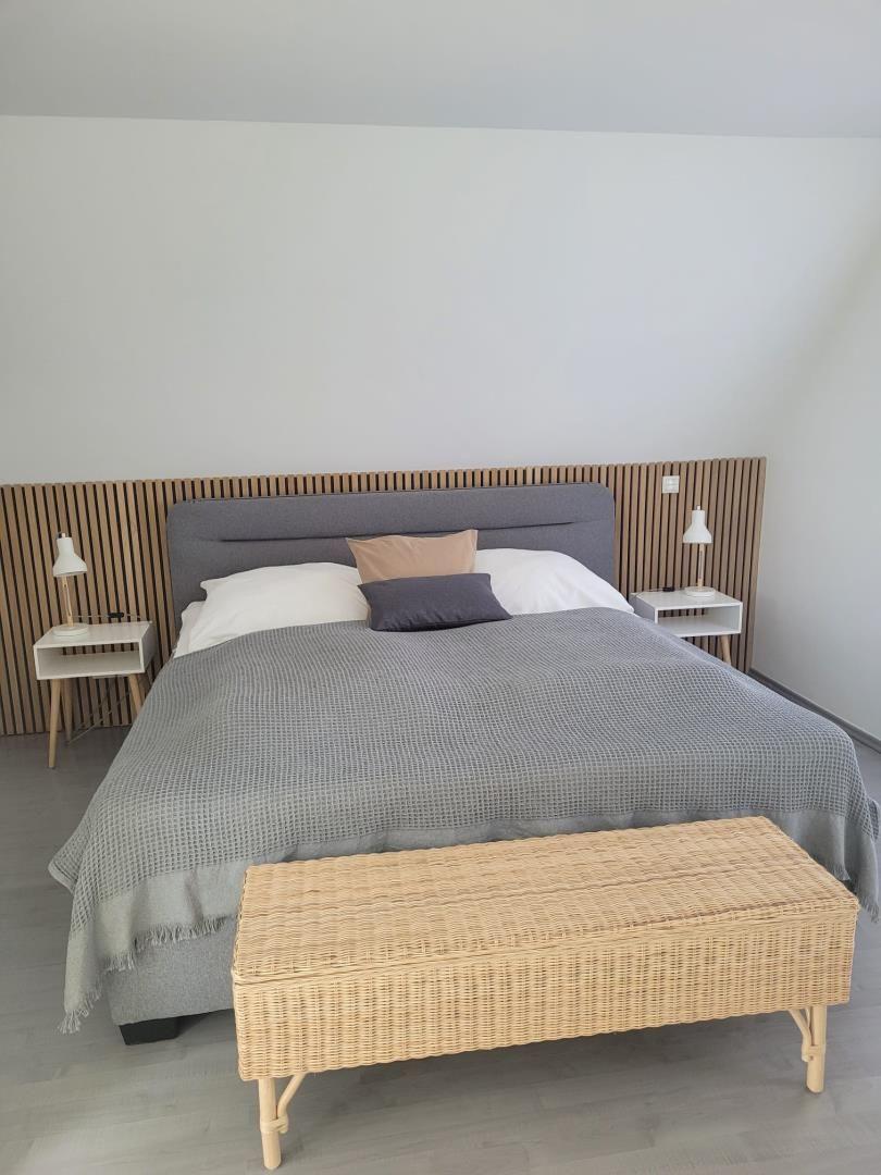 Doppelbett mit grauer Bettwäsche, zwei Nachttische und einem geflochtenen Sitzkasten.