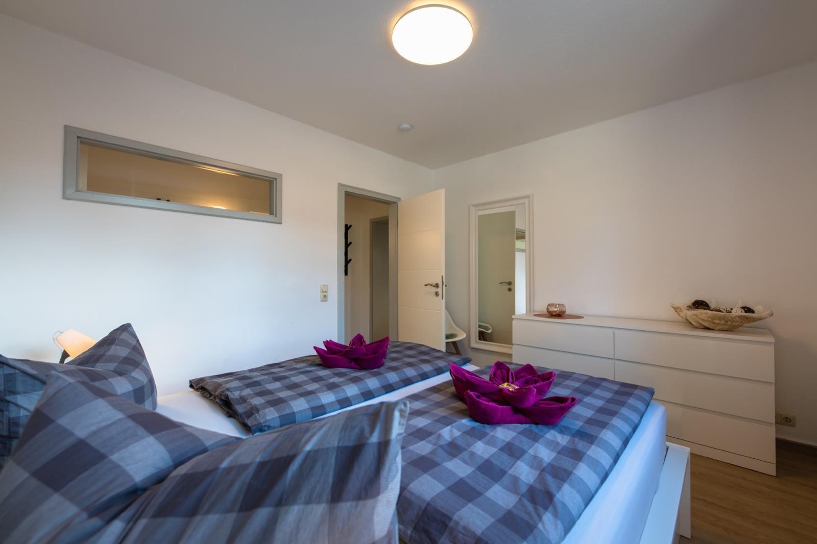 Schlafzimmer mit Bett, Schrank und Spiegel. Auf dem Bett liegen gefaltete Handtücher.