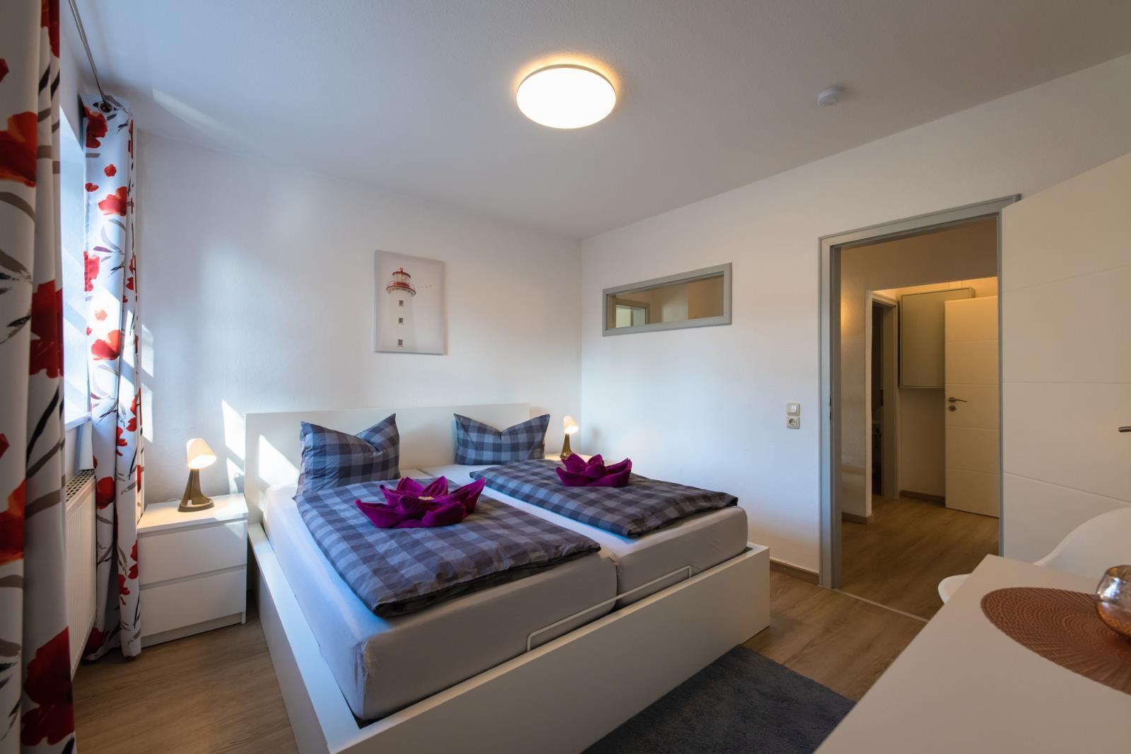 Schlafzimmer mit Doppelbett, Nachttischen und Fenster mit floralen Vorhängen.