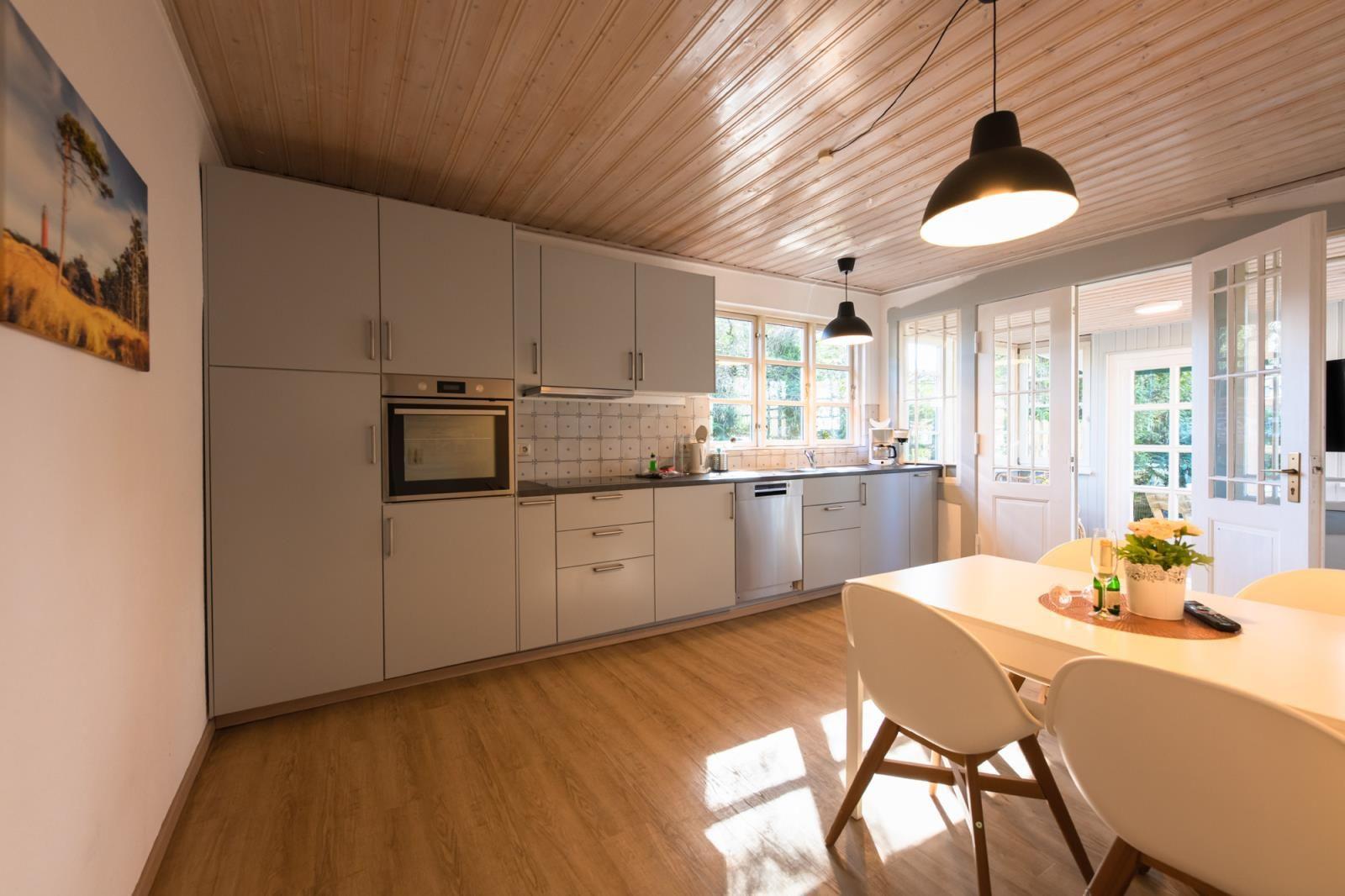 Küche mit Essbereich, Holzdecke und Fenstern. Tisch mit Stühlen und Blumenvase.