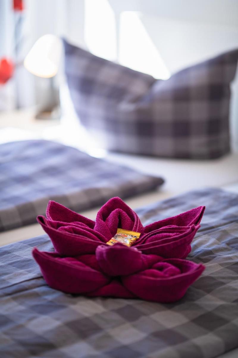 Ein rotes Handtuch in Form einer Blume liegt auf einem Bett mit kariertem Bettzeug.