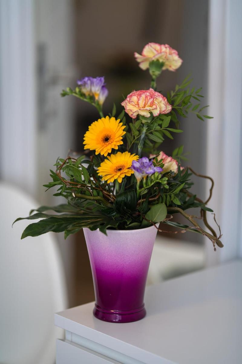 Blumenstrauß in einem lila-gelben Vase auf weißem Tisch