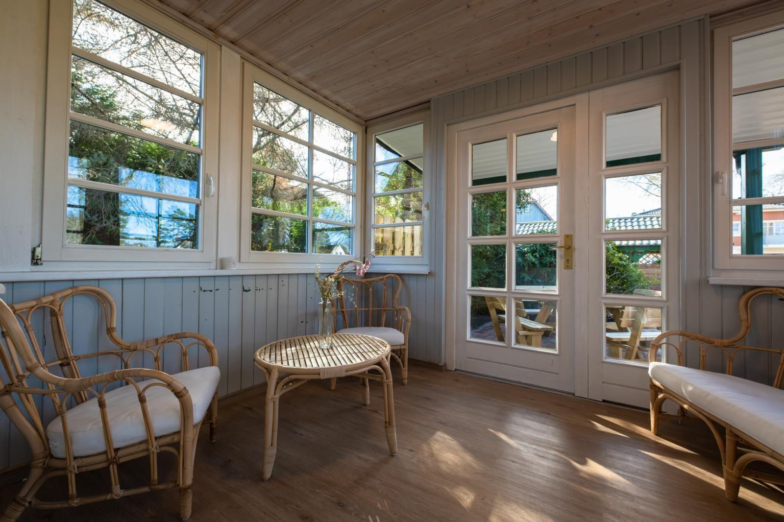 Terrassenbereich mit Rattanmöbeln und Holzboden. Große Fenster und Türen bieten Blick auf Garten.