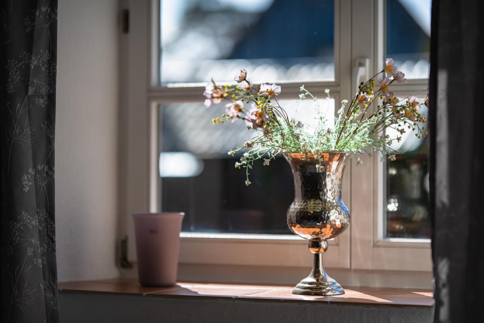 Ein silberner Vasenstrauß mit Blumen steht auf einem Fensterbrett.