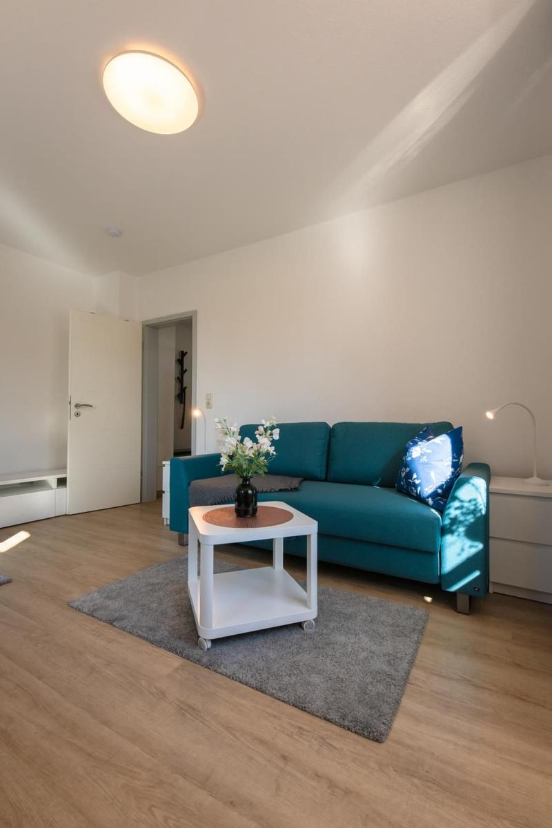 Ein Wohnzimmer mit einem türkisen Sofa, einem weißen Couchtisch und einem grauen Teppich.