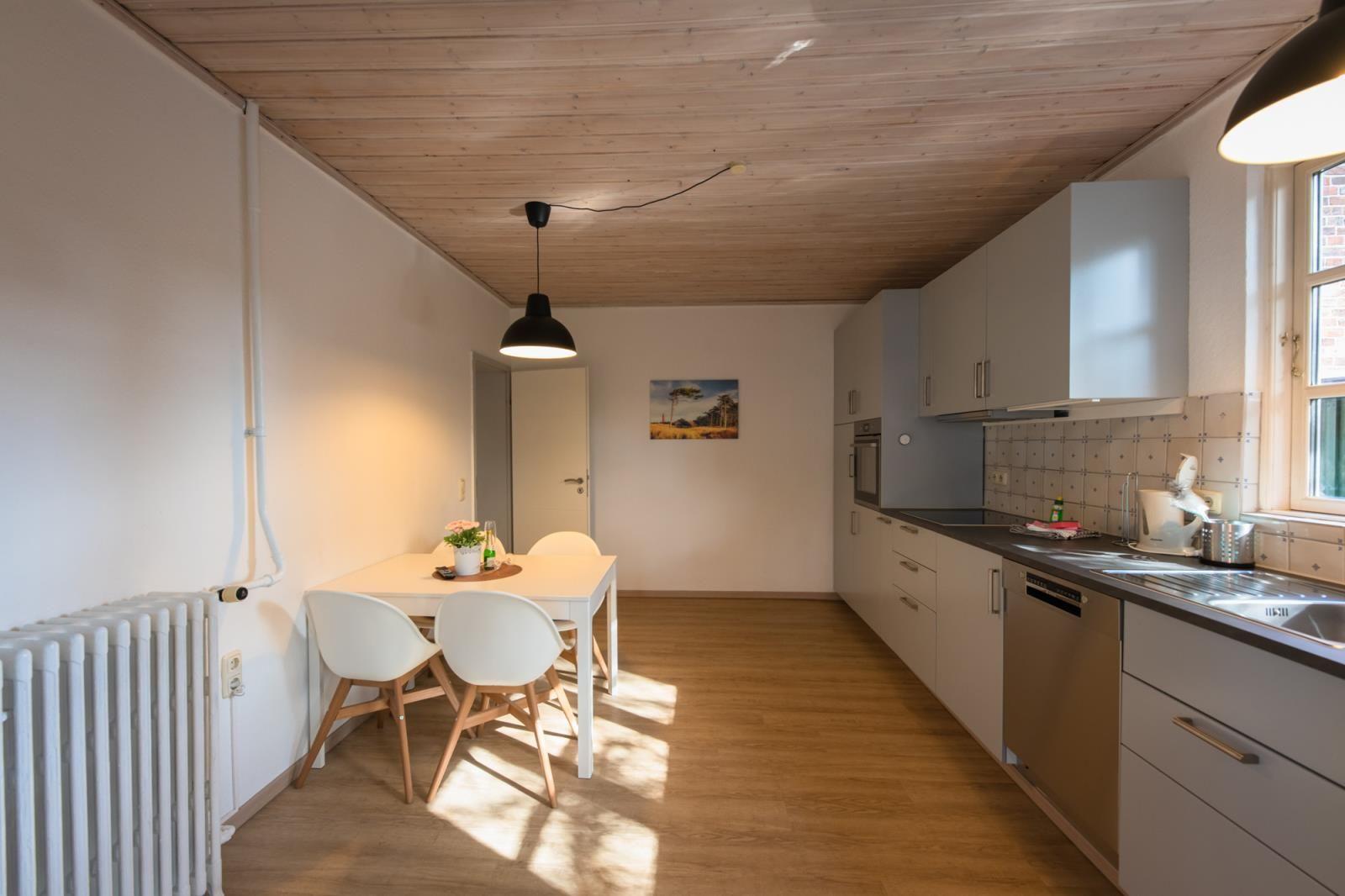 Küche mit Essbereich, Holzboden und Holzdecke. Weiße Möbel und Fenster.