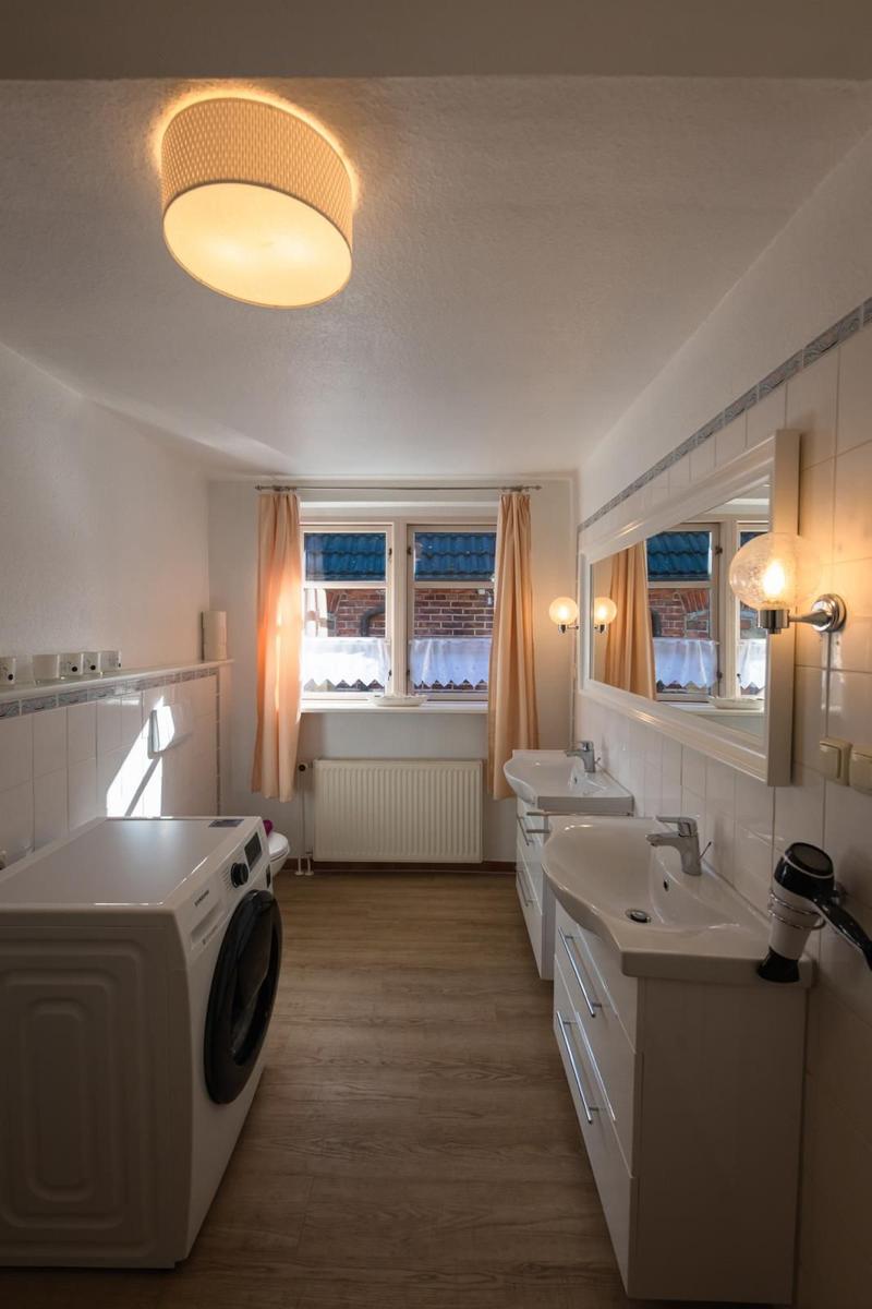 Badezimmer mit Waschmaschine, zwei Waschbecken und Fenster mit Vorhängen.