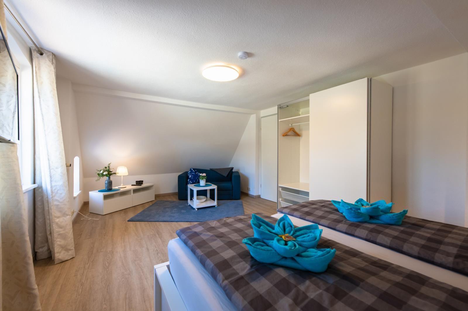 Room with two beds, wardrobe, and seating. Blue towels as decoration.