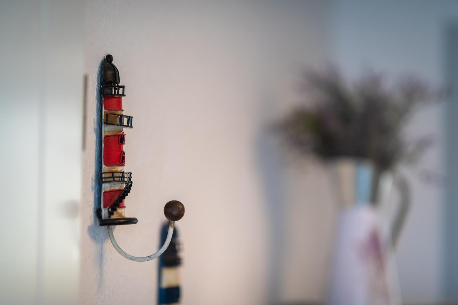 Wall-mounted lighthouse-shaped hook. A vase with flowers is in the background.