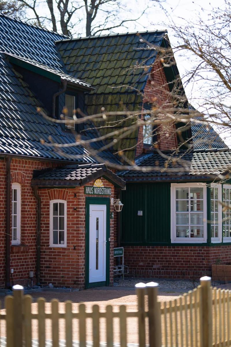 Haus Nordstrand with red brick, green roof, white door, and white windows.