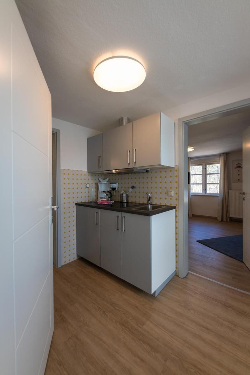Kitchen with worktop, sink, and cabinets. Background: living room with window.