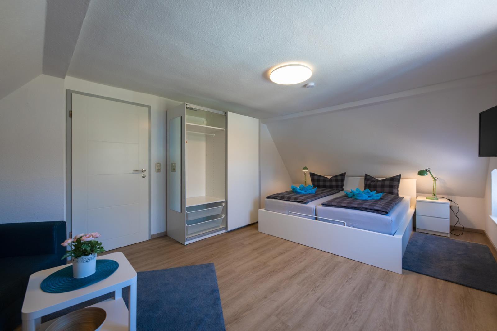 Bedroom with double bed, wardrobe, and TV. Wooden floor and blue rugs.