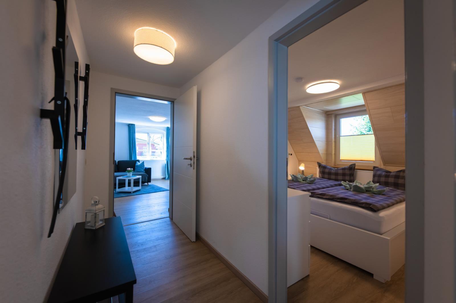 Flur mit Schlafzimmer und Wohnzimmer im Hintergrund. Holzfußboden und moderne Beleuchtung.