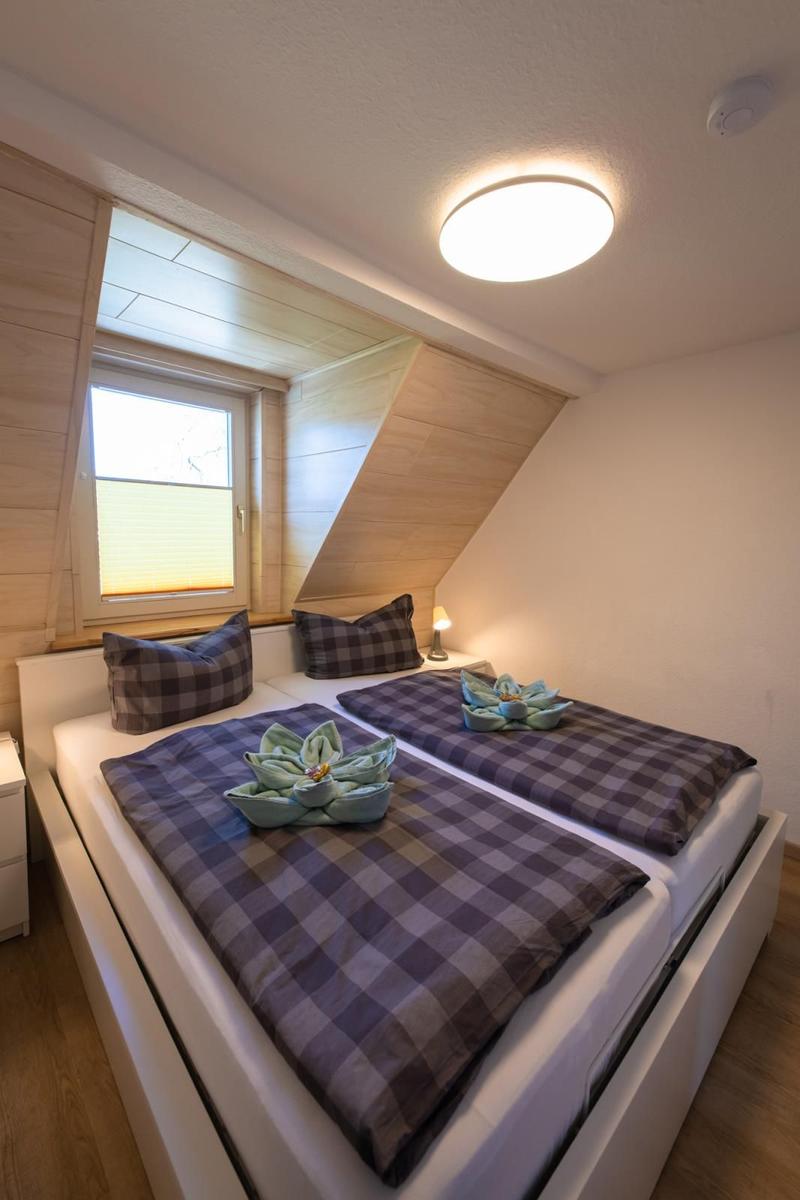 Schlafzimmer mit Doppelbett, Fenster und Deckenleuchte.