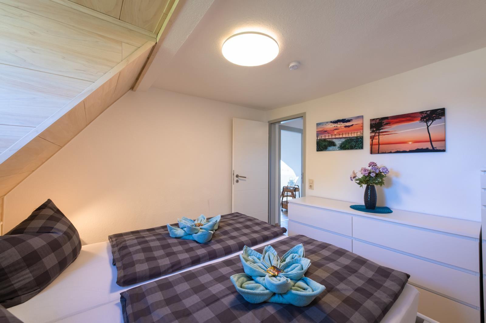 Schlafzimmer mit Doppelbett, Holzdecke und Wandbildern. Blumen auf Schrank.