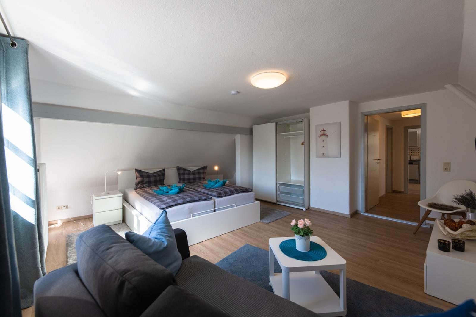Schlafzimmer mit Doppelbett, Wohnbereich und Blick in die Küche.