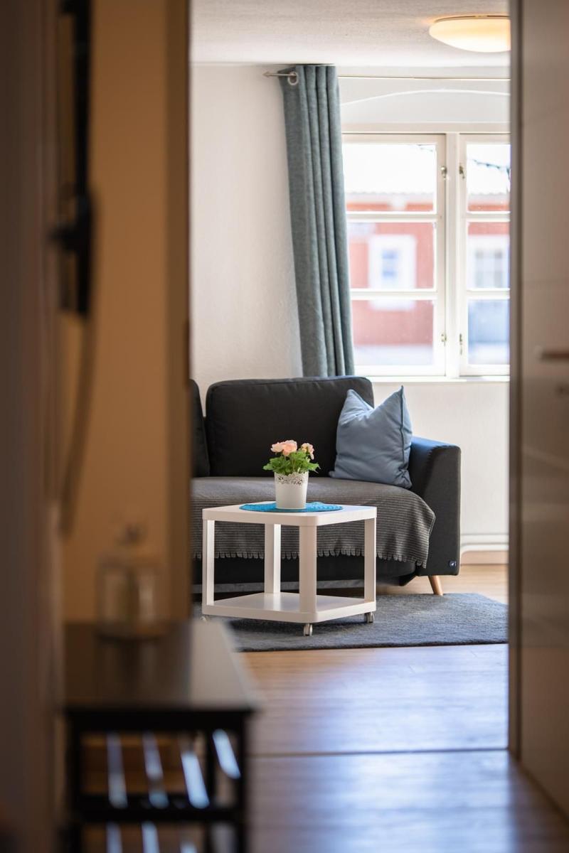 Ein Wohnzimmer mit grauem Sofa, blauem Kissen und kleinem weißen Tisch.