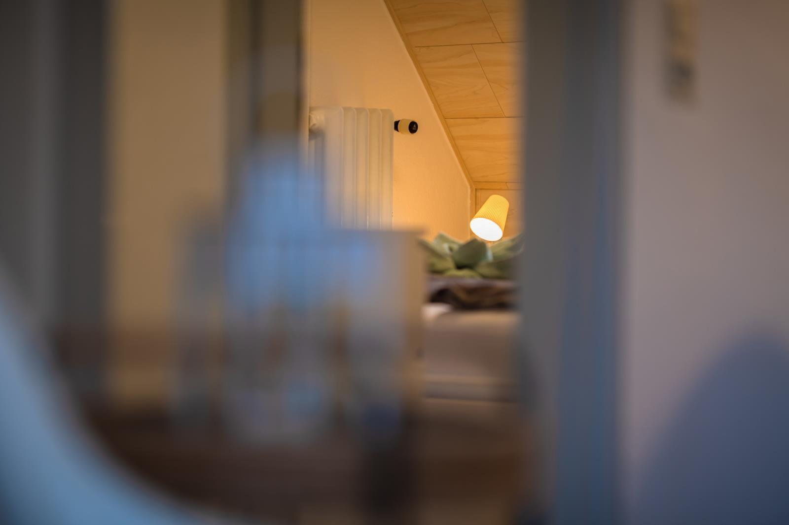 Ein Blick in ein Schlafzimmer mit Bett, Lampe und Heizkörper unter schrägem Dach.