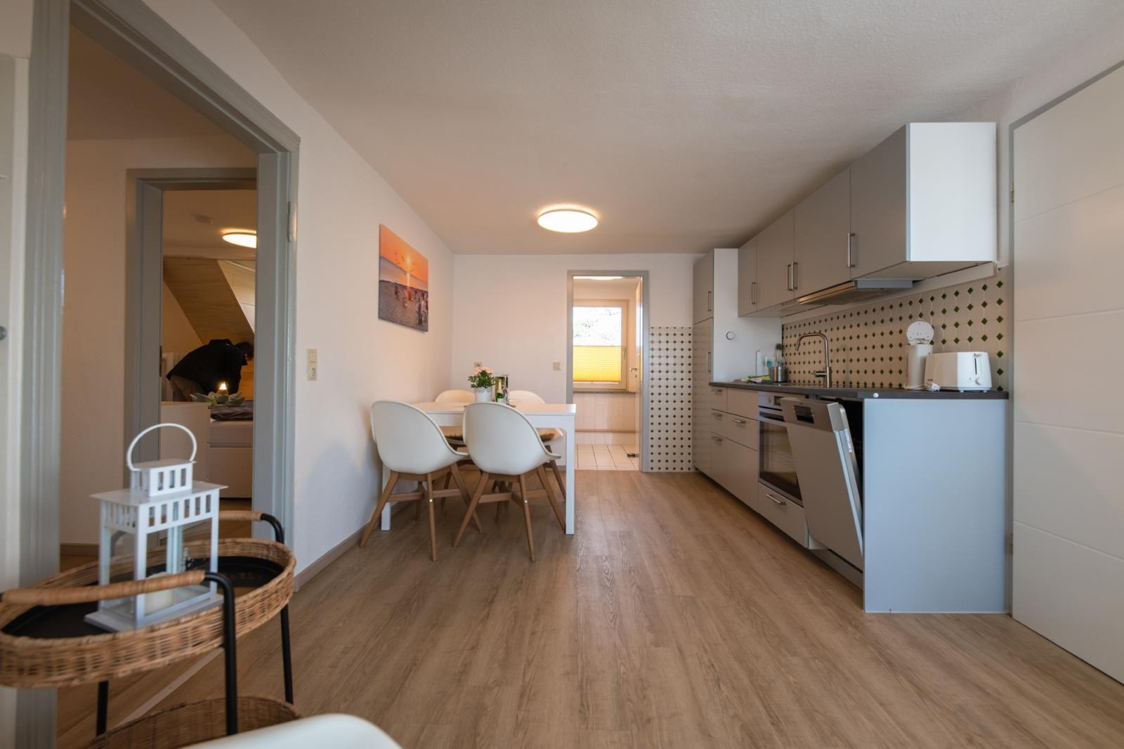 Küche mit Esstisch und Stühlen. Holzdielenboden. Blick in Schlafzimmer.