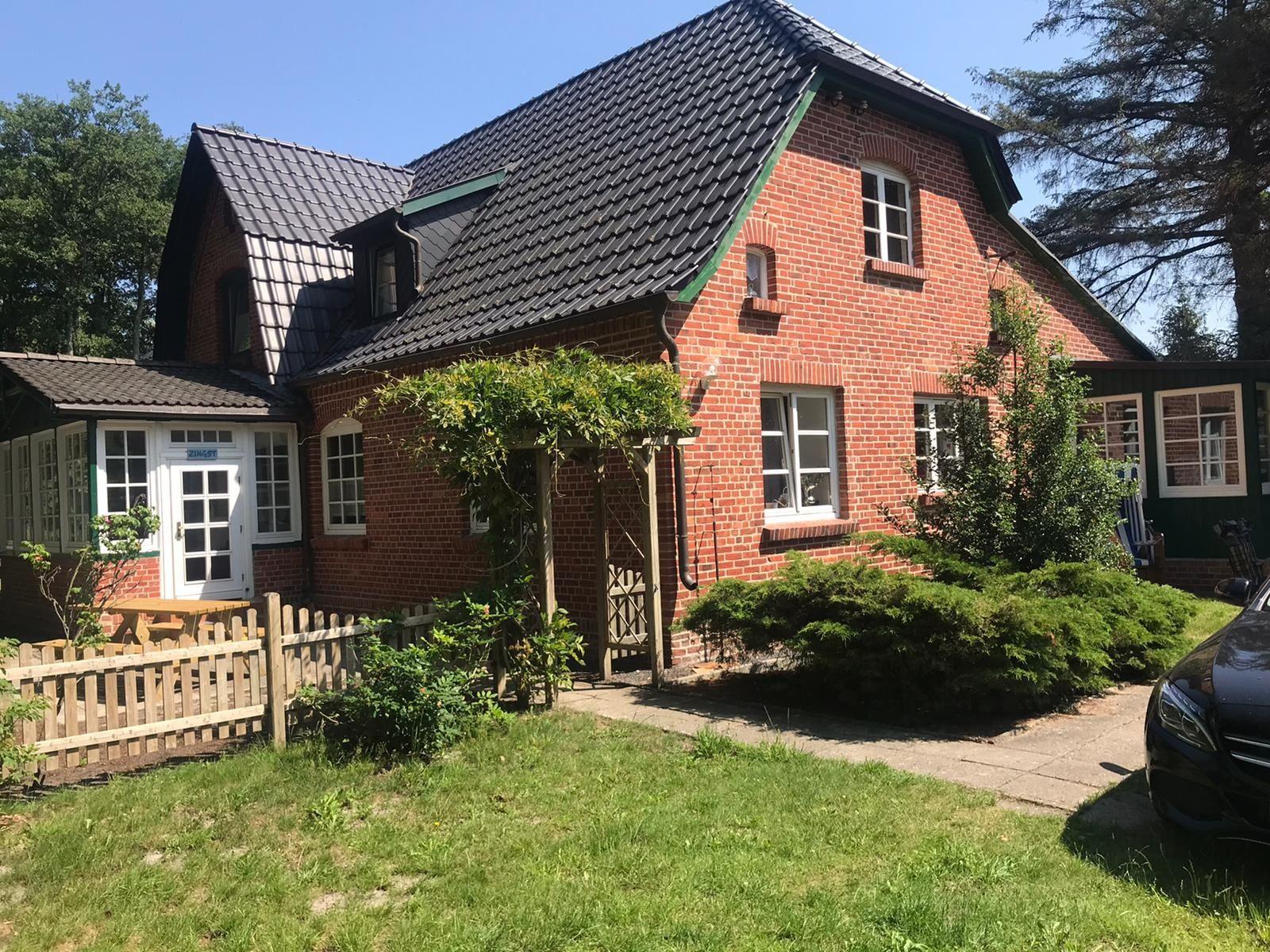 Red brick house with green roof and garden area with wooden gate and table.