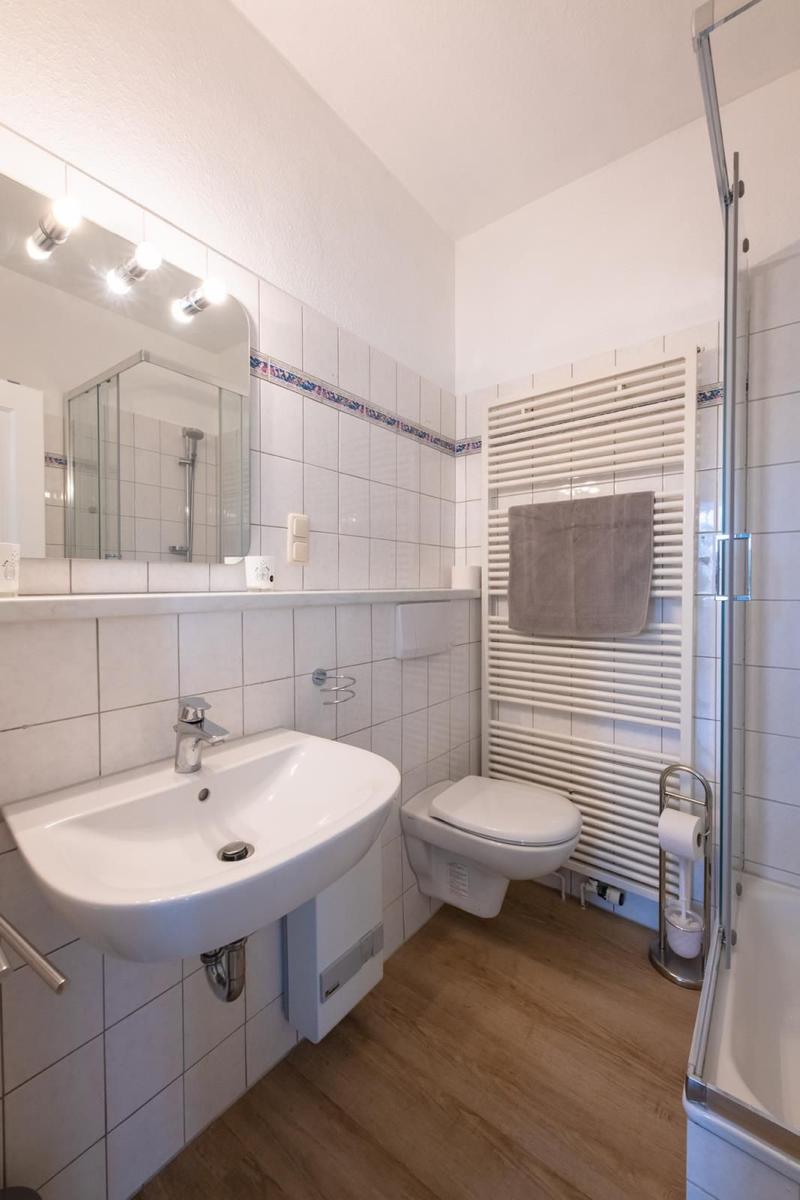Bathroom with sink, toilet, and shower. Tiled wall and wooden floor.
