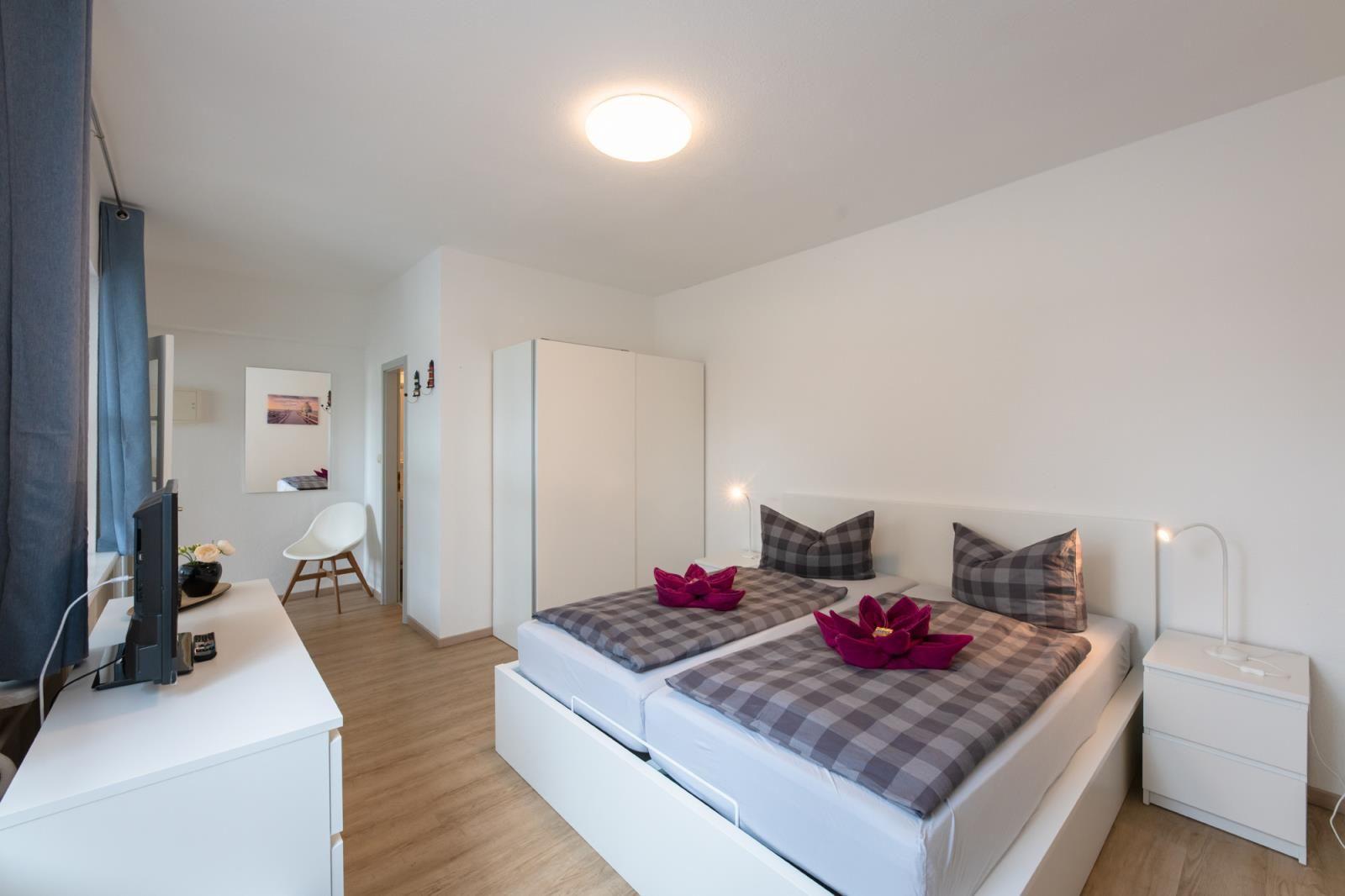 Bedroom with double bed, nightstand, and wardrobe. Window with curtains and TV table.