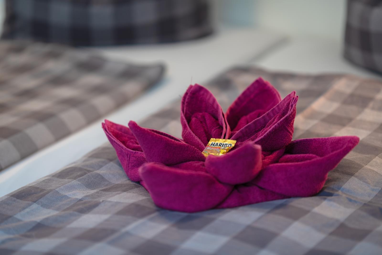 A purple towel flower on a checkered bedspread with a small candy.