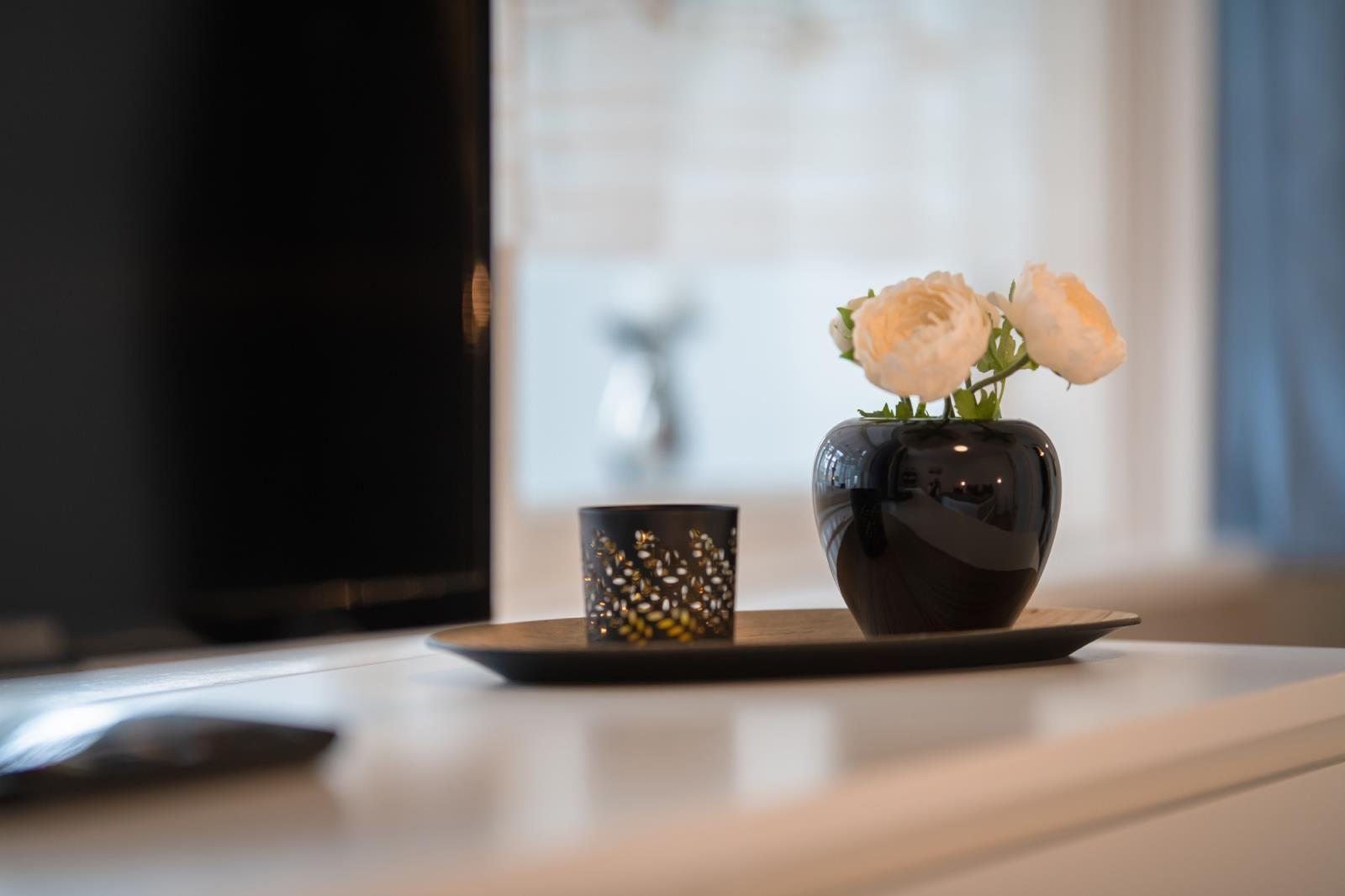 On the table, there is a vase with white flowers and a tea light candle.
