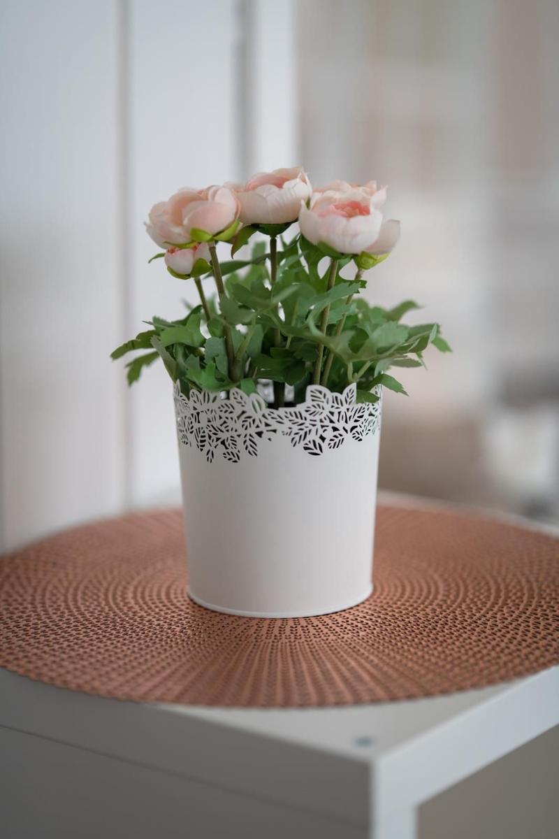 A white vase with pink flowers sits on a round, rose-colored mat.