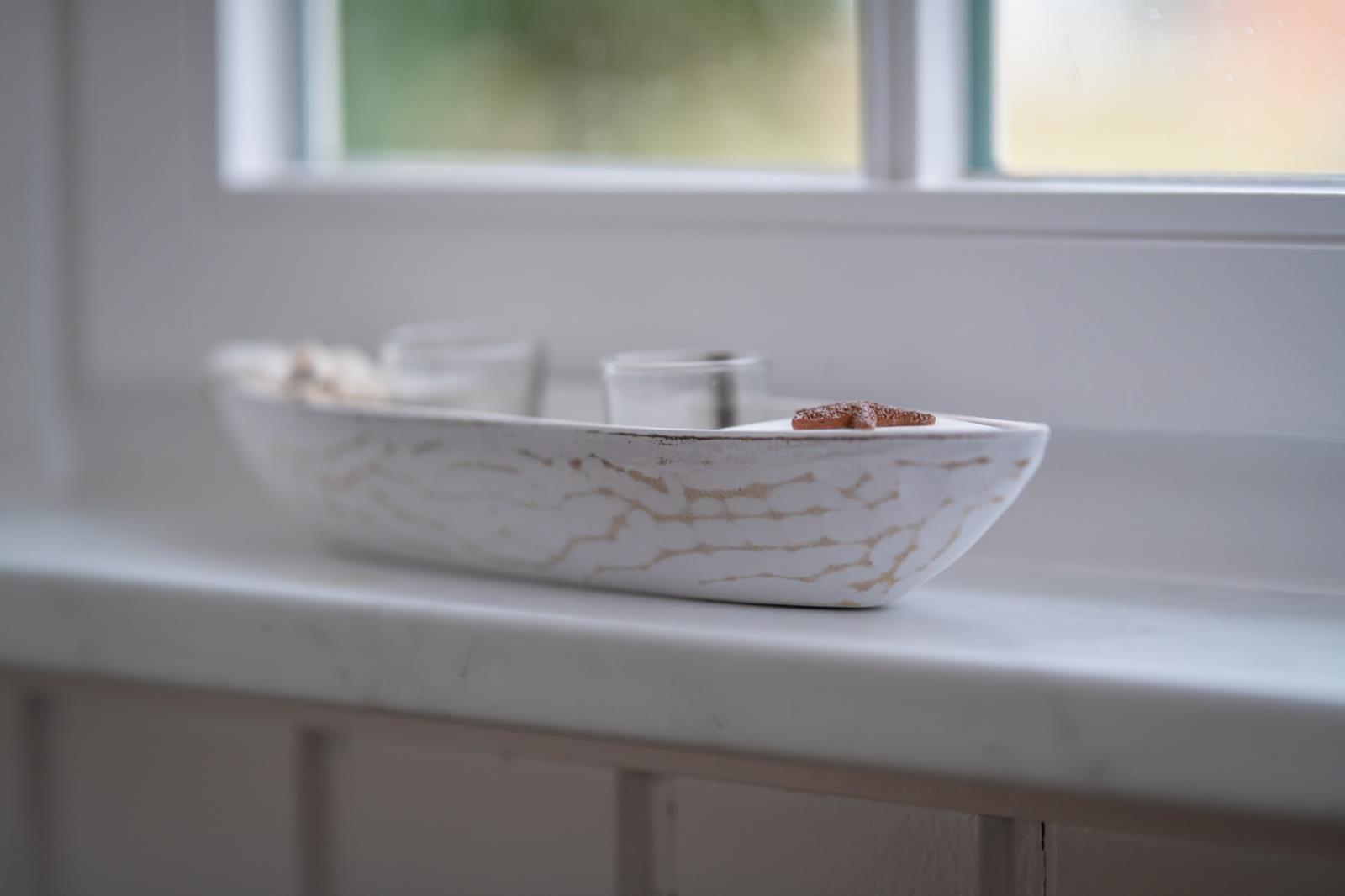 A white boat with a starfish and candle holders sits on the windowsill.