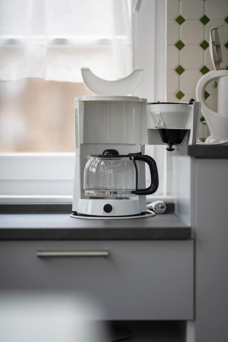 Coffee maker on kitchen counter next to window with green-white tiles
