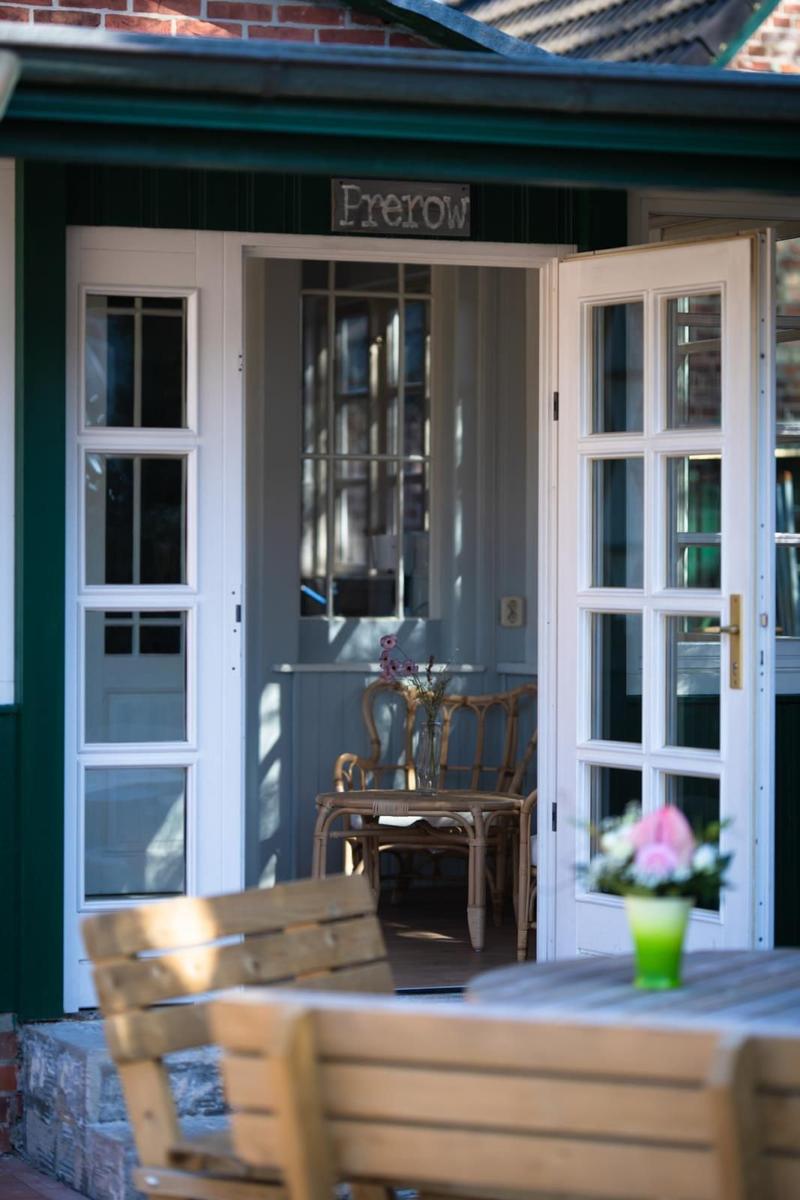 House with open door, wooden table and chairs in the garden. View into interior with table and chairs.